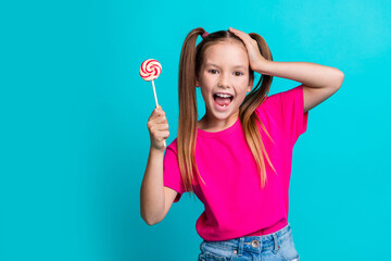 Photo of impressed overjoyed schoolgirl with ponytails wear pink t-shirt hold lollipop arm on head...