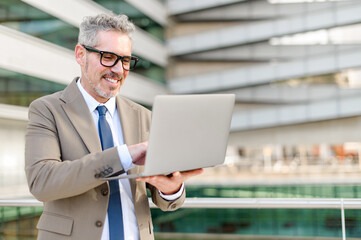 The experienced businessman is captured in mid-gesture, interacting with his laptop screen, against...