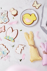 Pastel easter cookies and handmade easter rabbit made of cotton and wool on white wooden table flat lay