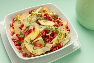 Fennel and apple salad with dill and pomegranate arils on a white plate.