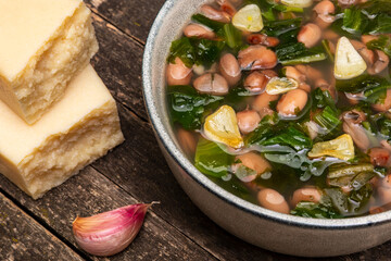 Escarole and pinto beans soup with fried garlic in bowl. Garlic cloves and chunks of parmesan on the side.