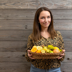 A young woman holds a wicker basket with an assortment of fruits (whole and halves). Healthy...