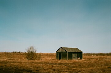 Fototapeta premium Old wooden house in a field with dry grass - film photo