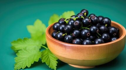 Black currant berries in a wooden bowl on a green background. Fresh black currant background. Top view. Close up of fresh black currants background. Healthy food concept