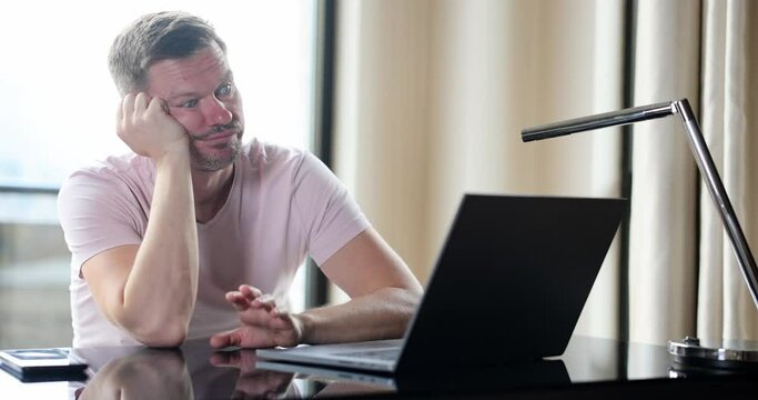 Bored young man sitting at table and waiting for message on laptop screen 4k movie slow motion. Poor internet quality concept