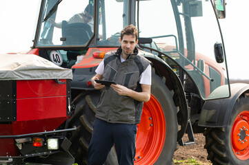 Young farm worker next to tractor using digital tablet