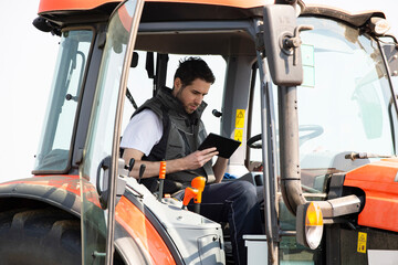 Young farm worker on tractor using digital tablet