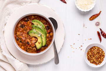 Top down view of a bowl of chili topped with avocado slices and chili flakes.