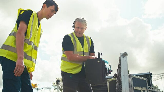 Production Team Unpacking Lights From Flight Case And Setting Up Outdoor Stage For Music Festival 