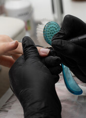 Beauty concept. A manicurist in black latex gloves gives a hygienic manicure to a client in a beauty salon. Close-up. Vertical.