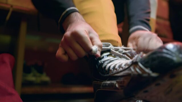 Ice hockey player ties the laces on his worn out, shabby skates in locker room before a game. Cloakroom indoor. Man get dressed and puts on his sports uniforms, tracksuit in dressing room. Close up