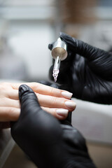 Beauty concept. A manicurist in black latex gloves makes a hygienic manicure and paints the client's nails with gel polish and drips oil on the cuticles in a beauty salon.