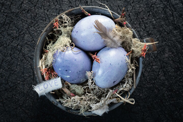 Eggs dyed with natural dye made with blueberries nesting in an antique enamelware cup on a black background.