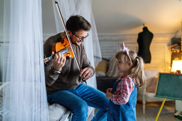 Happy family. Father and daughter playing on instrument together. Adult man playing violin for child