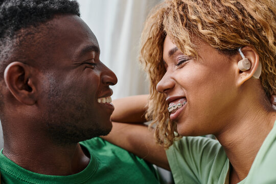 close up of happy deaf african american woman in hearing aid device smiling near boyfriend at home