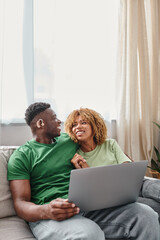 cheerful african american couple walking movie on laptop, deaf man in hearing air and woman