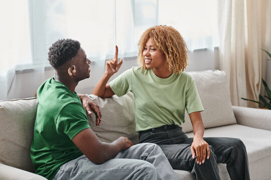 African American couple communicating with sign language on couch, black man in hearing aid