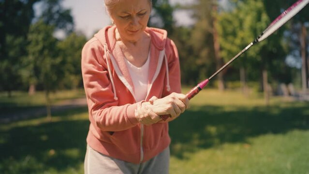 Senior woman playing badminton in park, feeling strong wrist pain, sports injury