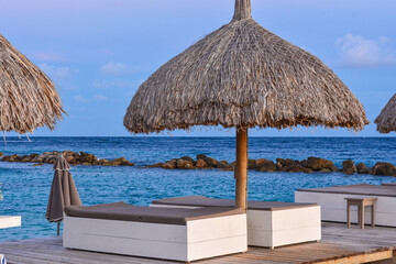 Palapa parasols and sun loungers on the jetty at the beach resort hotel on tropical Curacao island. 