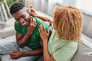 Obraz na płótnie Canvas deaf african american man smiling as his curly girlfriend assists with hearing aid, medical device