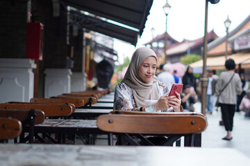 Indonesian Woman wearing Hijab Engaging in Digital Conversations at Cafe Bench