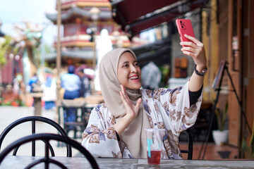 Indonesian Woman wearing Hijab Engaging in Digital Conversations at Cafe Bench