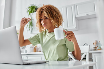 serious african american woman using sign language during video call and holding cup, nonverbal