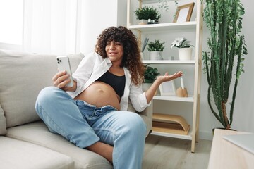 Pregnant woman blogger sits on the couch at home and takes pictures of herself on the phone, selfie...