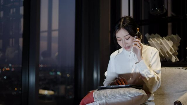 Happy young asian female freelancer at home office workplace at night. Smiling woman talking on mobile, using laptop and tablet, Working hard, small business and technology concept, working over time 