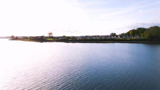 Malersiche Abendstimmung in einem schwedischen Feriendorf am Ufer eines ruhigen Sees mit farbenfrohen Holzh&auml;usern und einer Gr&uuml;nfl&auml;che. Drohnenaufnahme. Marina Fisken&aelig;s, Fisken&aelig;svej, Gr&aring;sten, D&auml;nemark