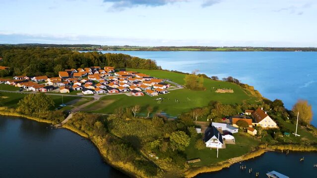 Luftaufnahme einer friedlichen Wohnsiedlung am Seeufer mit malerischer Landschaft und klarem blauen Himmel im Hintergrund. Drohnenaufnahme. Marina Fisken&aelig;s, Fisken&aelig;svej, Gr&aring;sten, D&auml;nemark