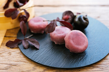 a black plate topped with pink balls and leaves on a wooden table. Mochi asian dessert