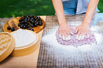 a person is kneading dough on a table with a bowl of cherries in the background. Mochi asian dessert