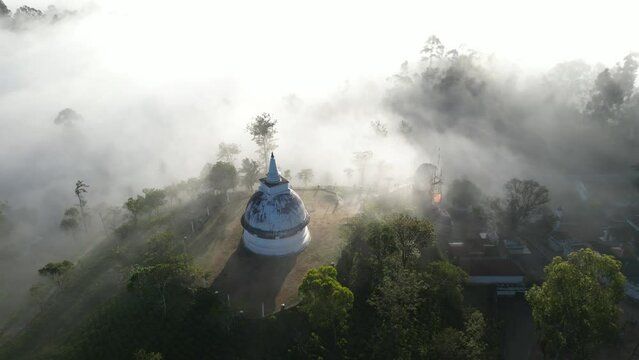 An old white buddhist temple stupa in the morning shine of sunbeams and clouds in the mountains and tropical jungle forest of Sri Lanka