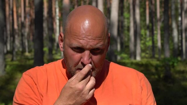 A man in an orange shirt is tasting or blueberries in a forest setting.