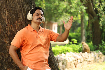 Portrait of a Indian man lost in music in calm green city park using head phones early morning...