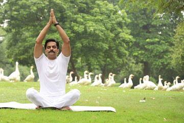 Happy Indian man doing yoga early morning in a tranquil environment surrounded with lush green...