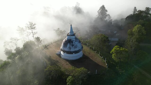 An old white buddhist temple stupa in the morning shine of sunbeams and clouds in the mountains and tropical jungle forest of Sri Lanka