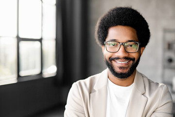 Young Brazilian businessman with a charming smile stands confidently, looking at the camera with friendly smile. The minimalist background emphasizes his modern approach to business and connectivity