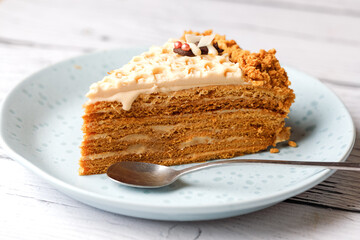 Piece of delicious layered honey cake with chocolate bee on white wooden background.