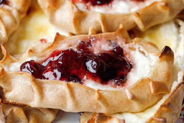 Karelian plays or Karjalanpiirakka. Traditional finnish or north russian pastry with cottage cheese and jam on clay plate. Close up.