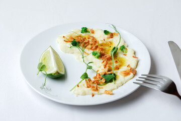 Garnish mashed potatoes with onion, sauce and micro greens, and slice of lime on white plate. Top view.