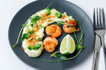 Scallops served with garnish mashed potatoes on black plate with fork and knife on white background. Top View.