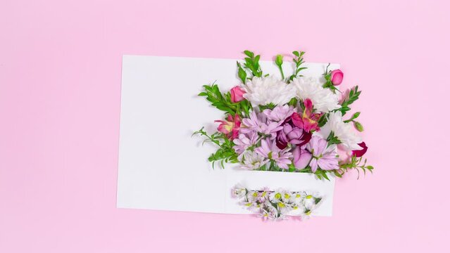 Beautiful bouquet of natural flowers appears in opening card. Pink background. Greeting card for birthday, mother's day, women's day or other occasion. Stop motion animation. Copy space. Flat Lay.