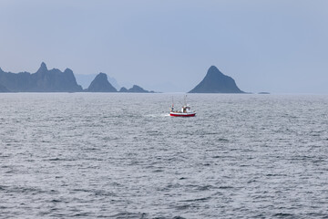 A solitary fishing boat cruises the waters near Andenes, against the dramatic silhouette of the Lofoten Islands in Norway.