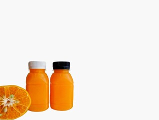 The white background in the picture is a bottle.The image has a white background and two small orange juice bottles with white and black caps close together. There is also a halved orange placed 