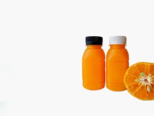 The white background in the picture is a bottle.The image has a white background and two small orange juice bottles with white and black caps close together. There is also a halved orange placed 