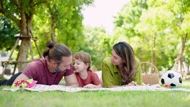 Caucasian family, parents children, was lying face down on mat spread on grass in garden near house, everyone had picnic on their free time, laying around chilling talking.