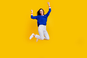 Full length photo successful champion woman jumping trampoline raised fists up triumphant and leader isolated on yellow color background