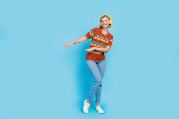 Full length photo of pretty girl wear strited t-shirt jeans in headphones dancing near empty space isolated on blue color background